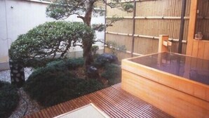 Un onsen japonés tradicional con una bañera de madera, una valla de bambú y un pequeño jardín.