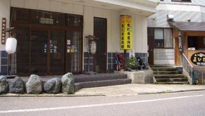 A building with a tiled facade, a wooden entrance, and a yellow sign. - Ryokan Tamanashi Onsen Ebisuya (Kaneyama)