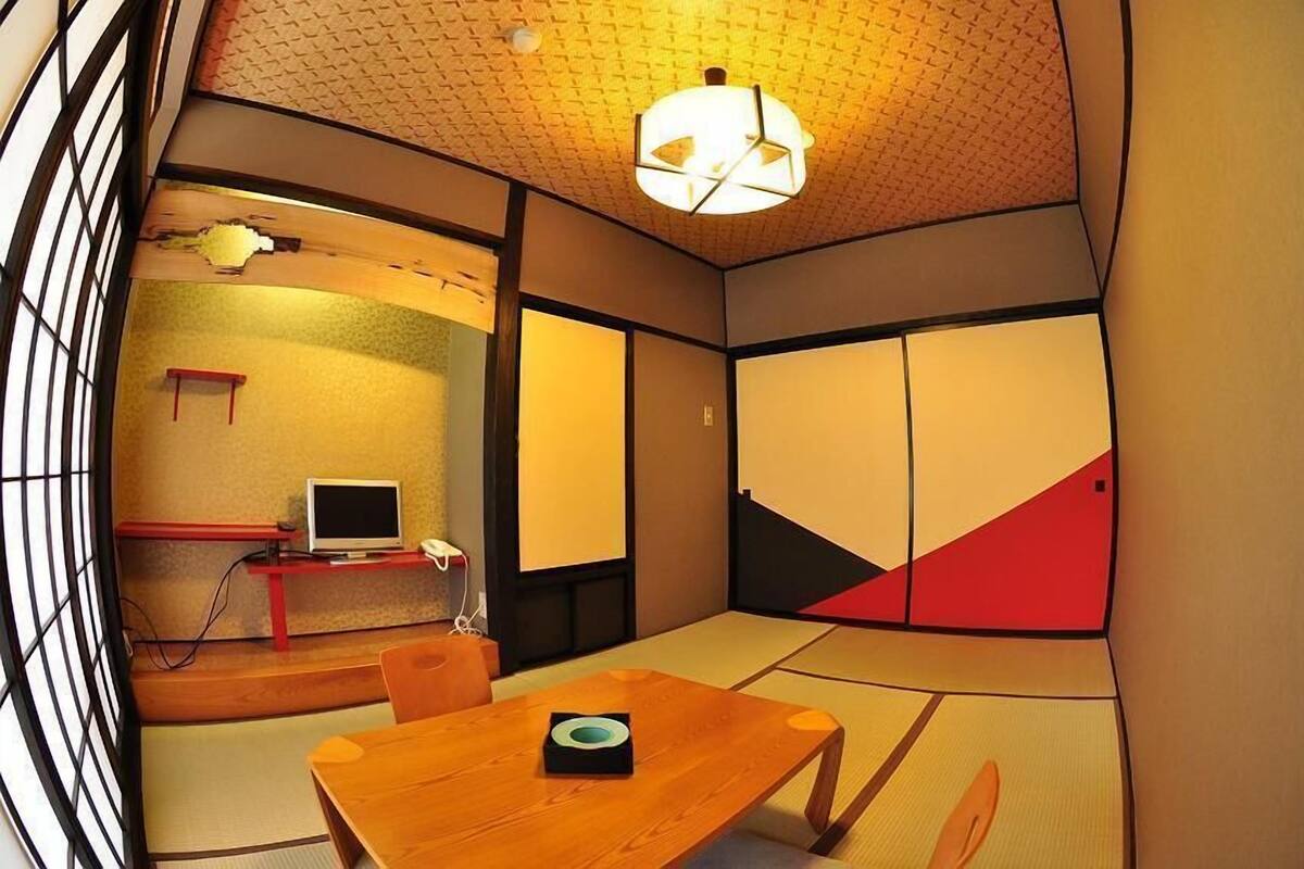 Une pièce de style japonais traditionnel, avec un sol recouvert de tatamis, une table basse, un téléviseur et des portes coulissantes.