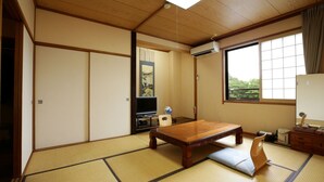 A traditional Japanese room with tatami flooring, a low wooden table, a television, and a large window with a view. - Yakushido Spa (Oshu)