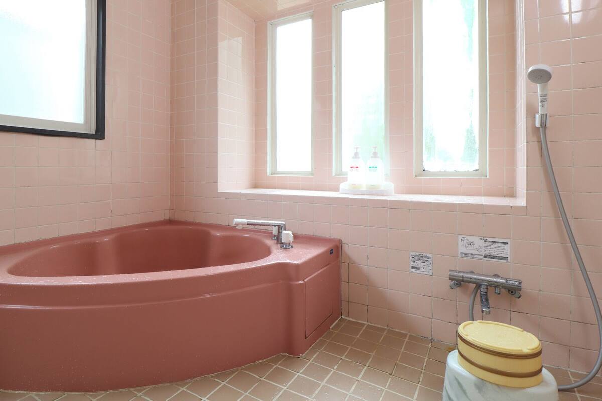 A bathroom with a red bathtub, a window with a view, and a shower.