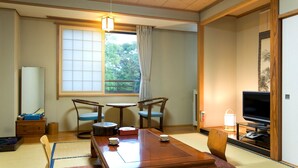 A traditional Japanese room with tatami flooring, a low table with a tea set, two wooden chairs, a television, and a sliding door. - Yakushido Spa (Oshu)