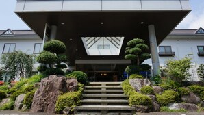 A modern building with a geometric entrance, stone steps, and surrounding greenery. - Yakushido Spa (Oshu)