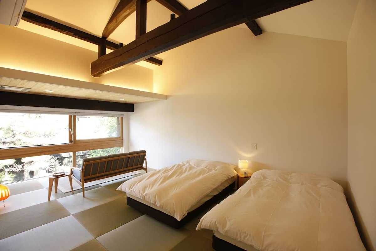 A room with two beds, a bench, a window, and a lamp.