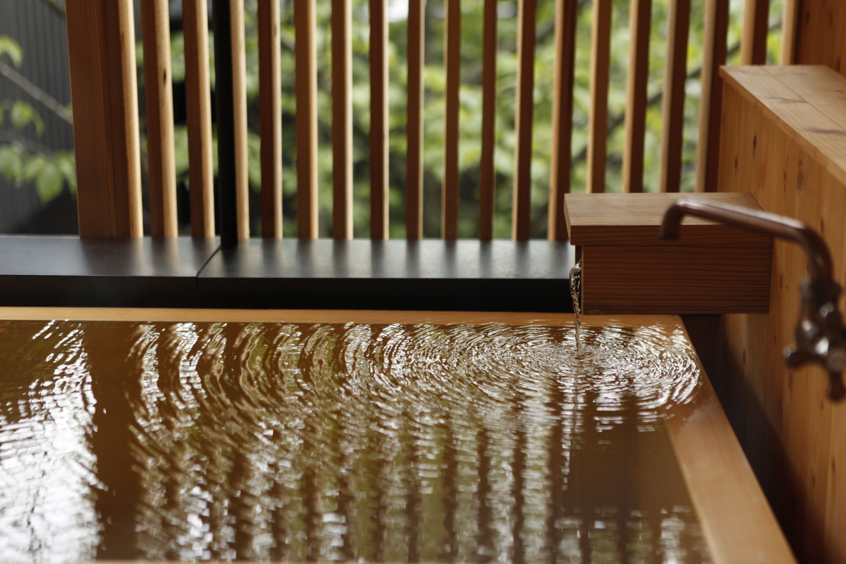 A wooden bathtub with a faucet, set against a backdrop of vertical wooden slats.