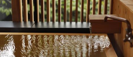 A wooden bathtub with a faucet, set against a backdrop of vertical wooden slats.