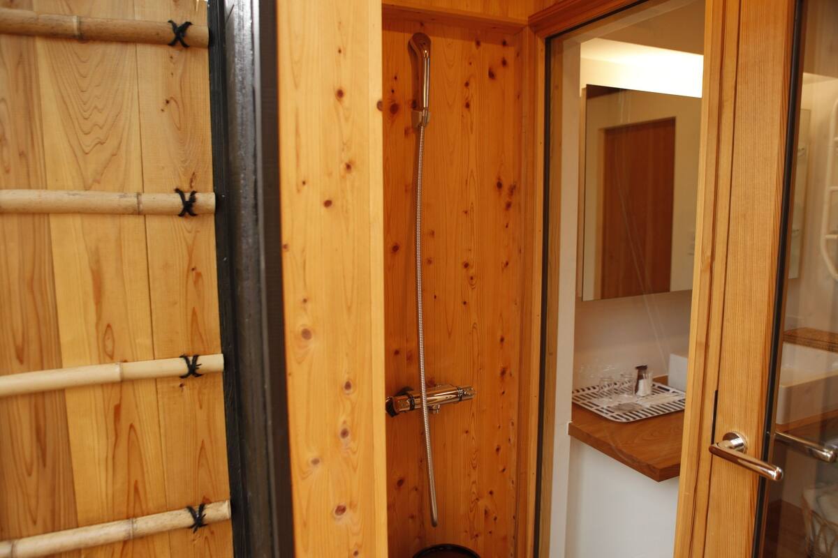 A wooden shower enclosure with a glass door, a showerhead, and a small shelf with toiletries.