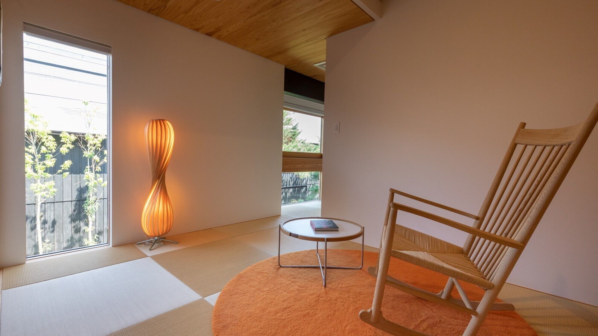 Una stanza con pavimento in tatami, una sedia di legno, un tavolino con un libro e una lampada da terra.
