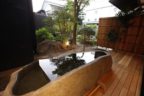 Ein Thermalbad mit einer Holzterrasse, einem Steingrundschale und umgebender Bepflanzung.