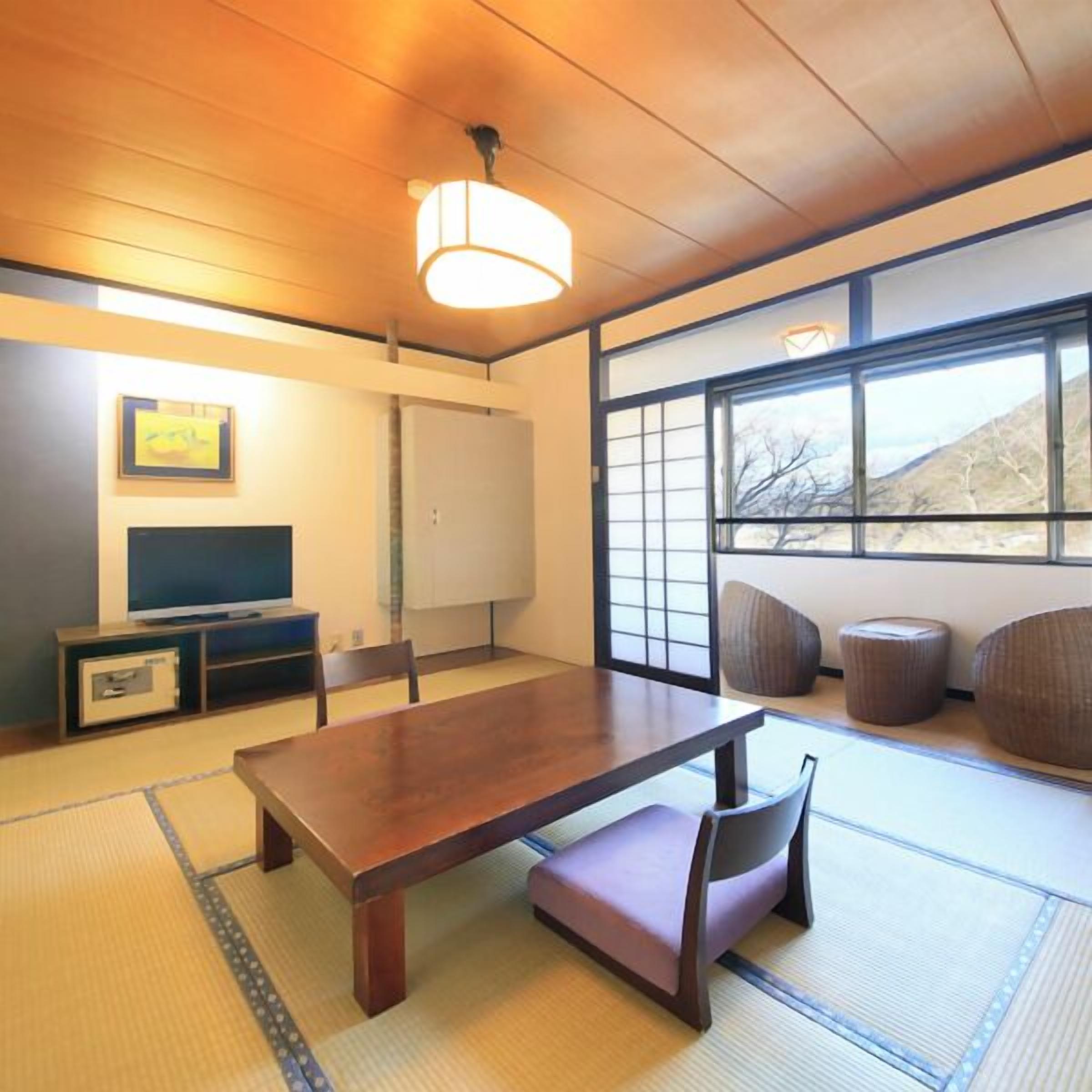 Une pièce de style japonais traditionnel, avec un sol recouvert de tatamis, une petite table basse, un téléviseur et une grande fenêtre donnant sur l’extérieur.
