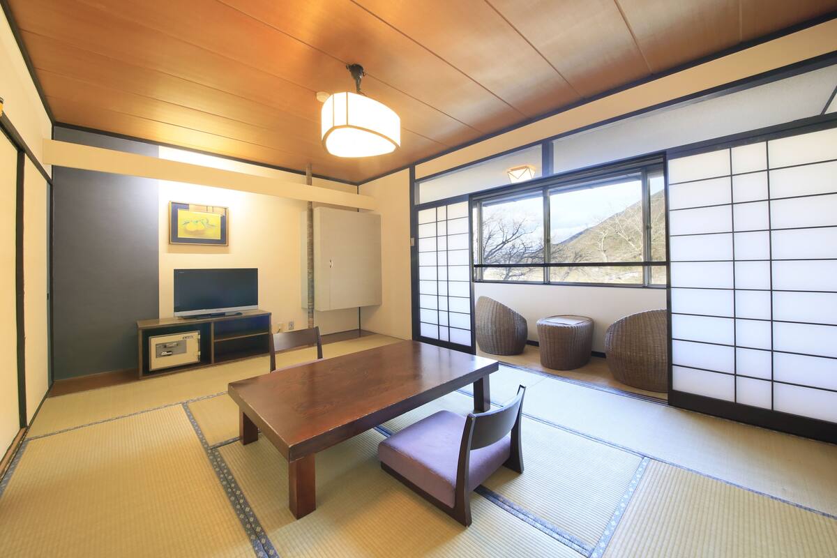 Una habitación japonesa tradicional con suelo de tatami, una mesa de madera baja, un televisor y un panel corredizo shoji.