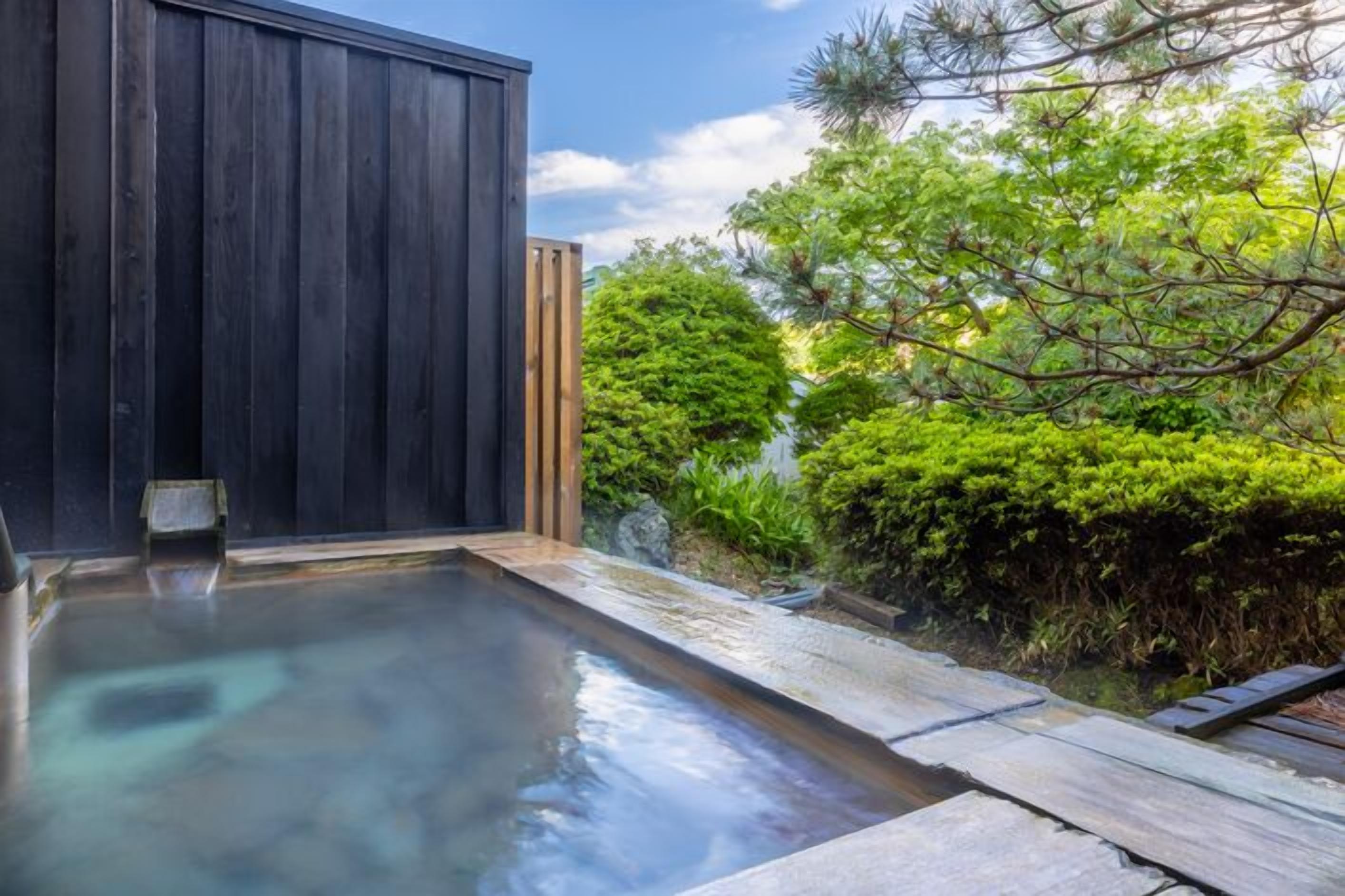 A modern outdoor pool area with a wooden deck and a dark wooden structure.