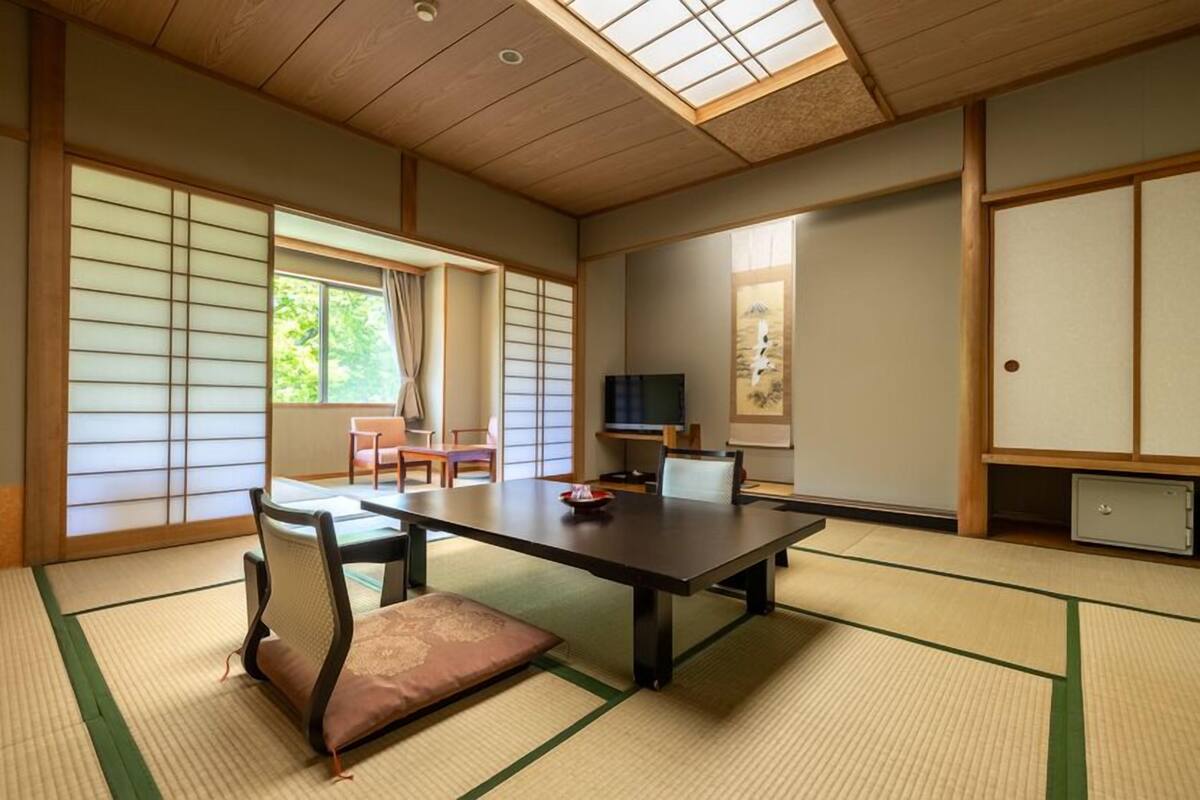 Una habitación tradicional japonesa con suelo de tatami, una mesa baja, sillas, un televisor y puertas correderas.