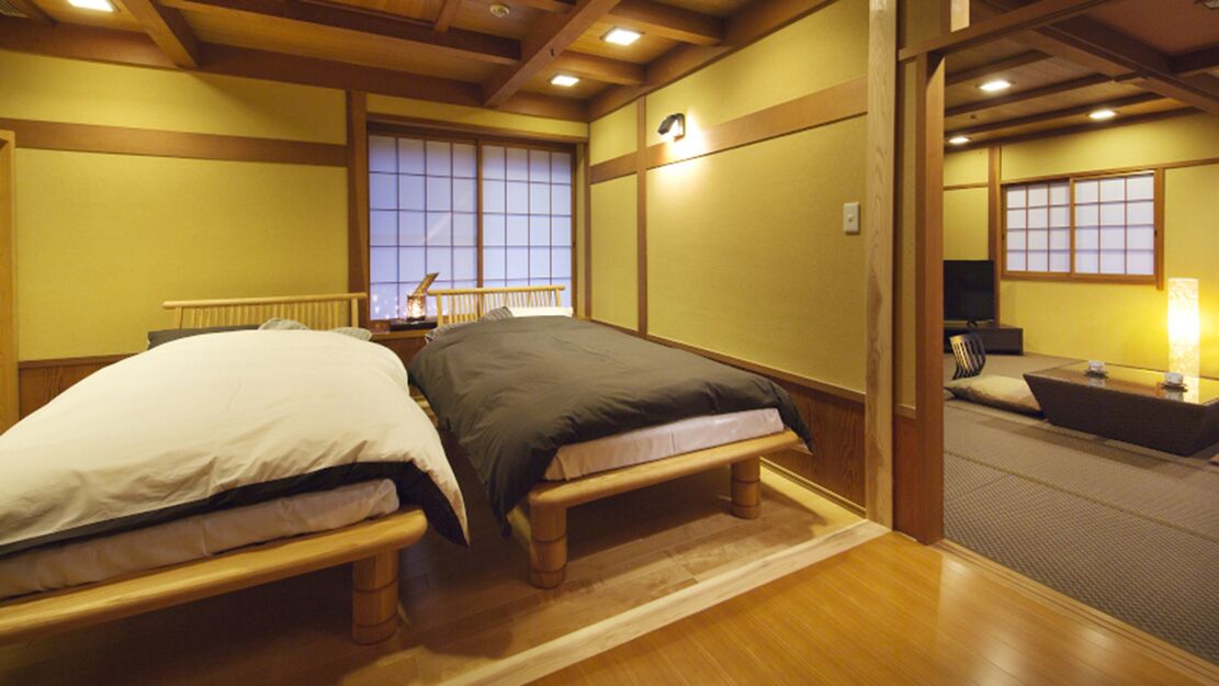 Une pièce de style japonais traditionnel, avec deux lits en bois, un sol recouvert de tatamis et des portes coulissantes.
