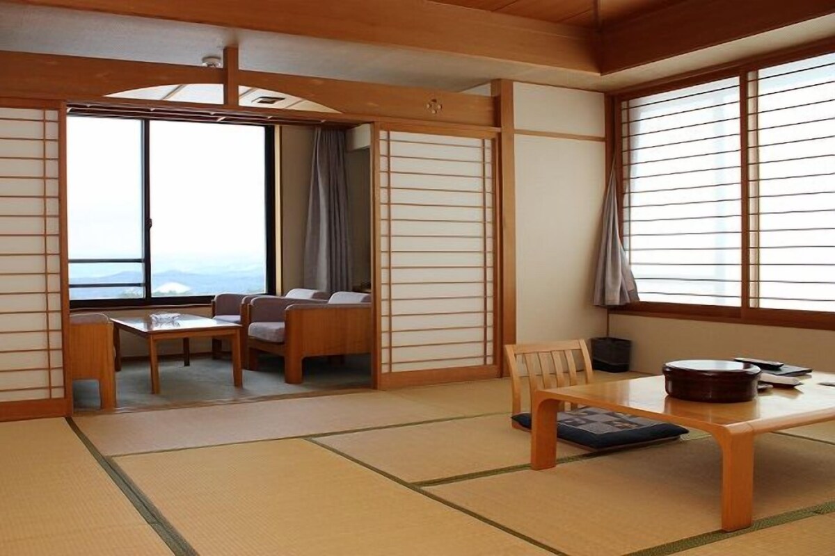 Um quarto japonês tradicional com tatames, uma mesa baixa, um sofá e vista através de uma grande janela.