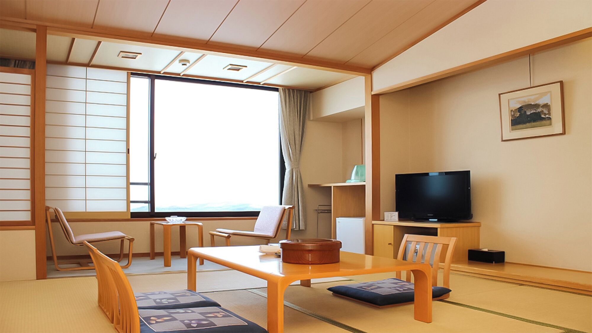 A traditional Japanese-style room with tatami flooring, a low table, chairs, a television, and a window with a view.