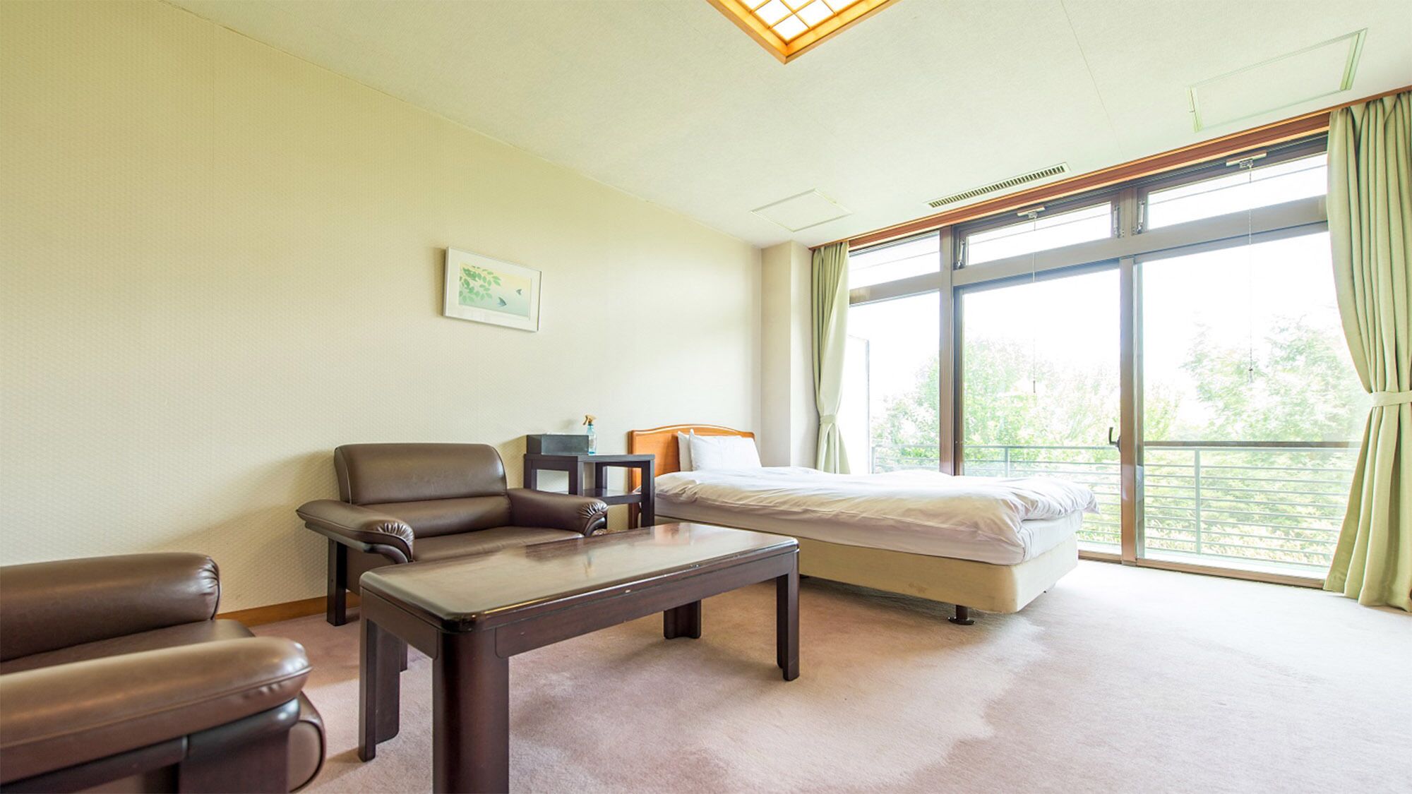 A hotel room with a bed, a sofa, a table, and large windows.