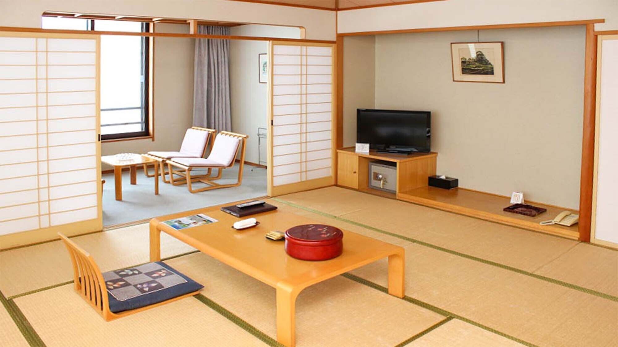 Een traditionele Japanse kamer met tatami vloerbedekking, een lage tafel met een rode container, een televisie en een schuifdeur.