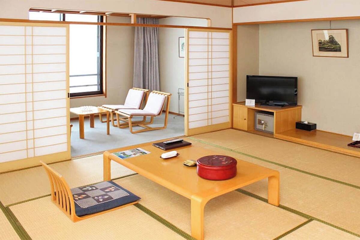 Una habitación japonesa tradicional con suelo de tatami, una mesa baja con un recipiente rojo, un televisor sobre un soporte de madera y una puerta corrediza con paneles shoji.