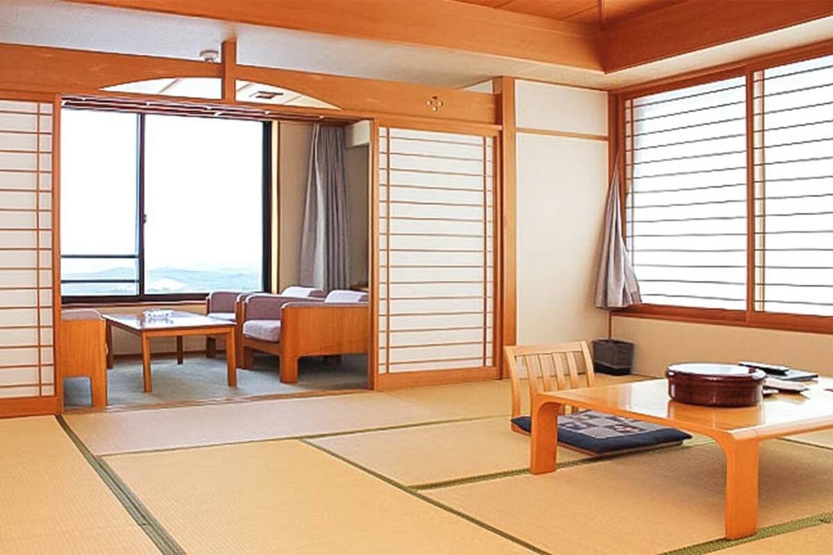 Una habitación tradicional japonesa con suelo de tatami, una mesa baja, sillas y puertas correderas.