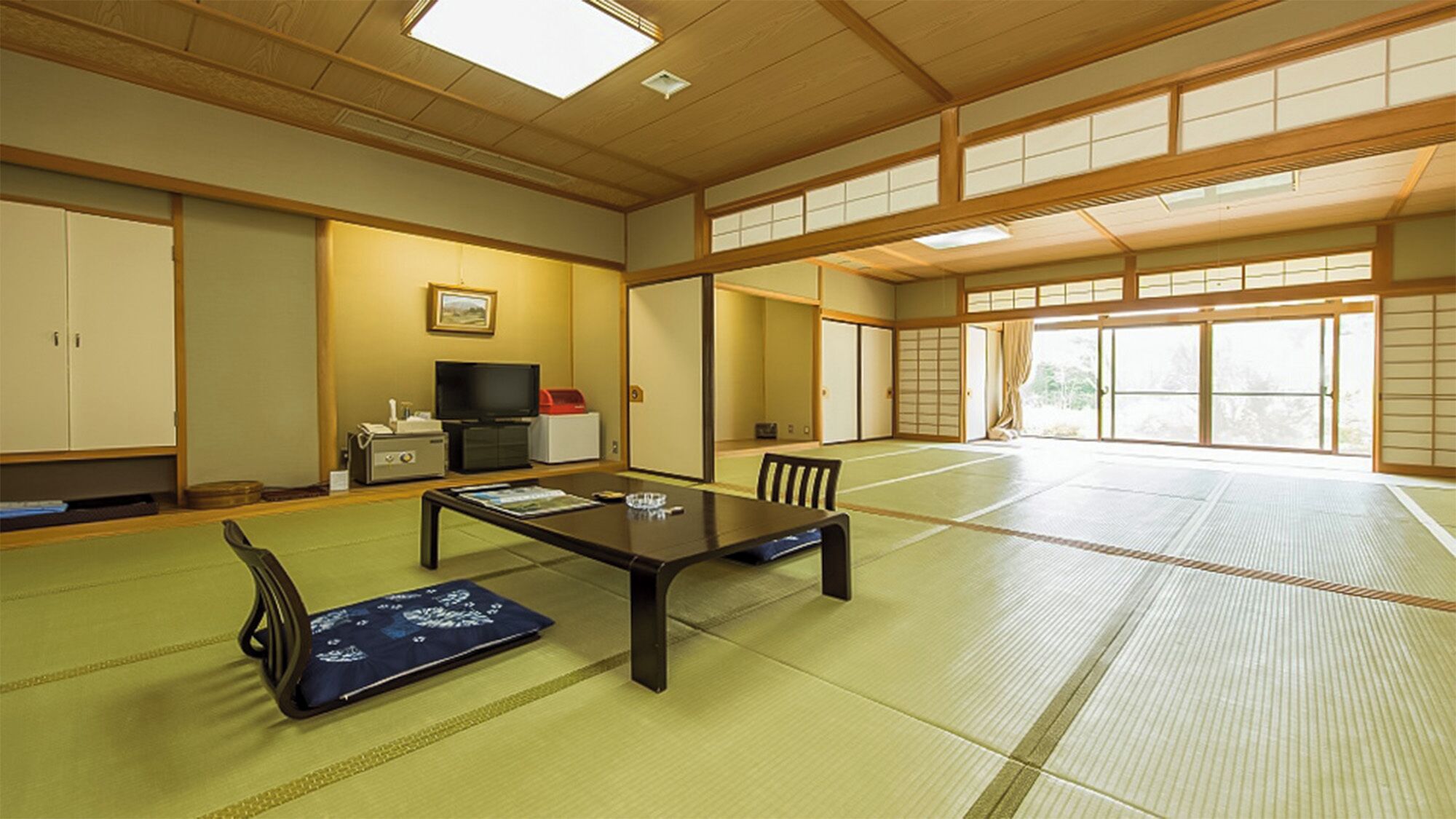 A tatami mat room with a low table, chairs, a television, and sliding doors.