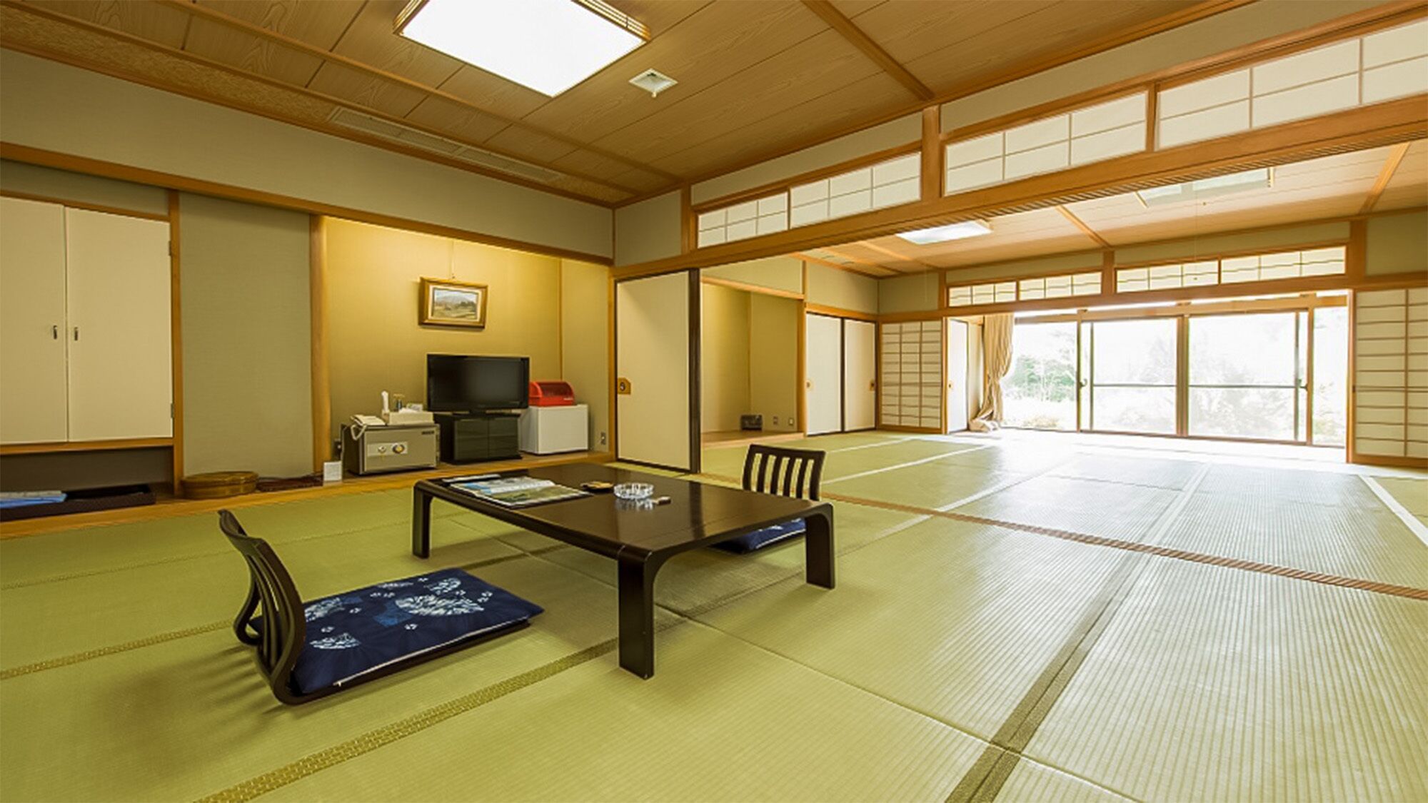 Een traditionele Japanse kamer met tatami vloerbedekking, een lage tafel, stoelen, een televisie en schuifdeuren.