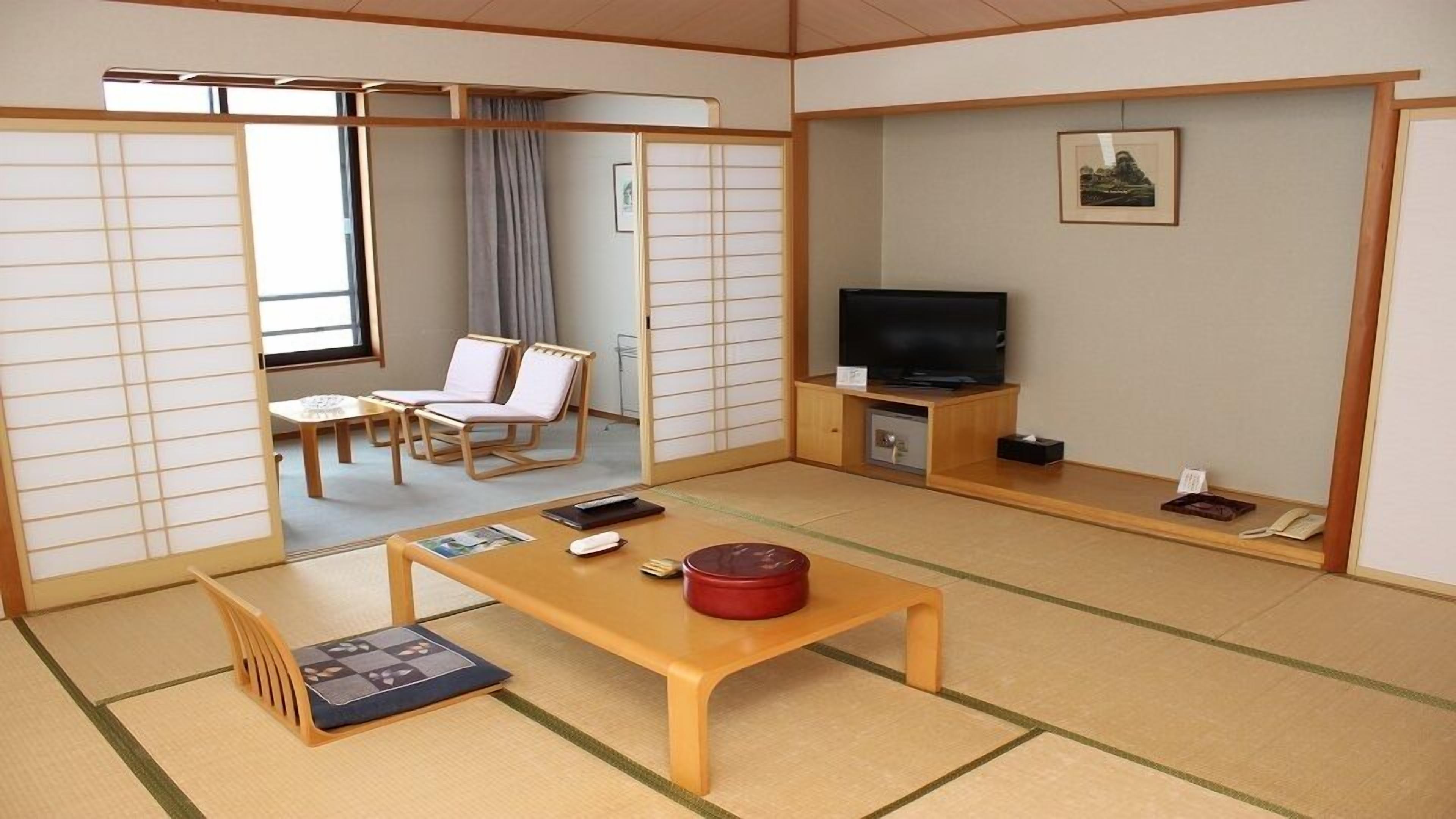 A traditional Japanese-style room with tatami flooring, a television, a small table with a red container, and a sliding door leading to a seating area.