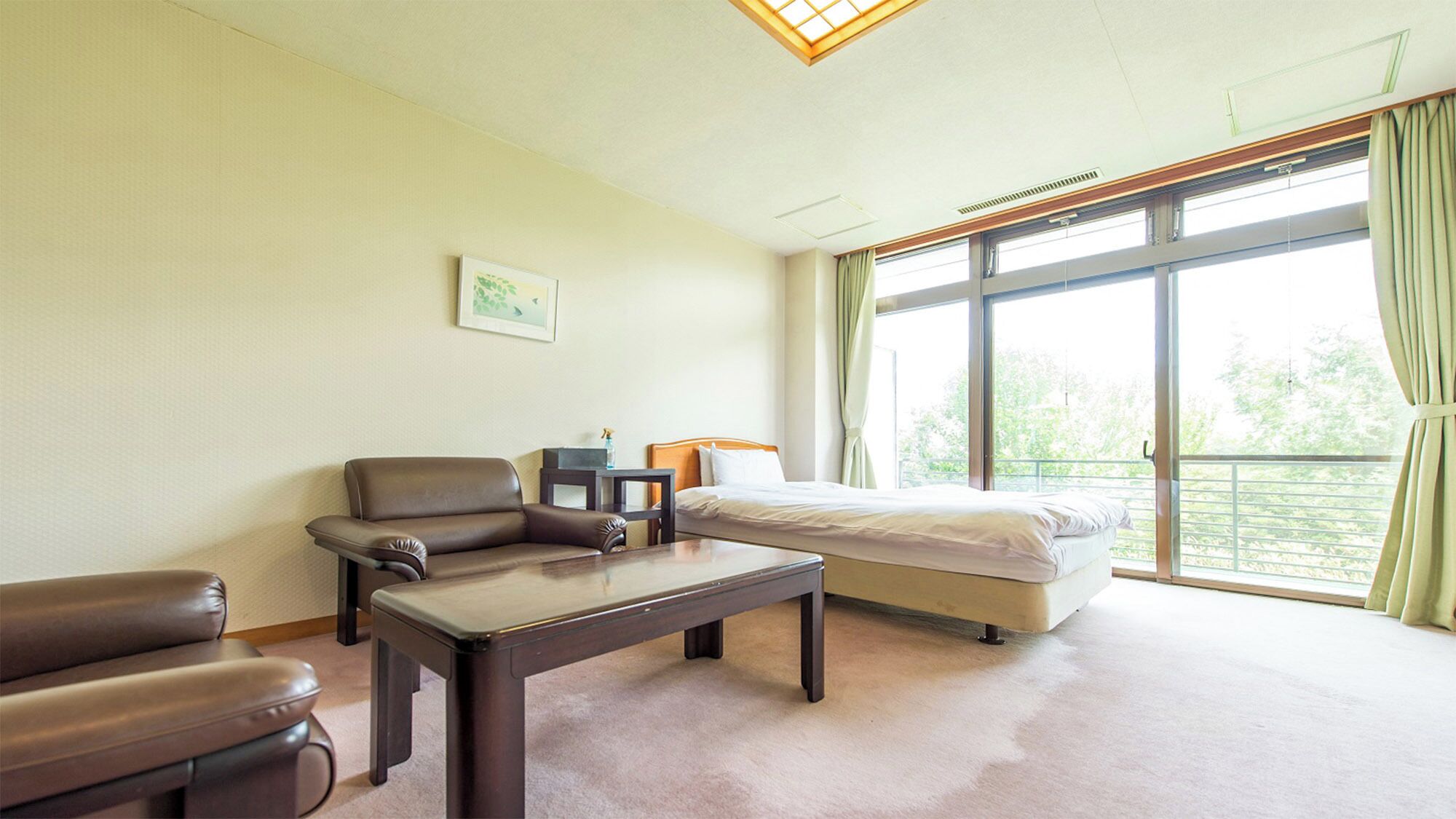A hotel room with a bed, a sofa, a table, and a large window with curtains.