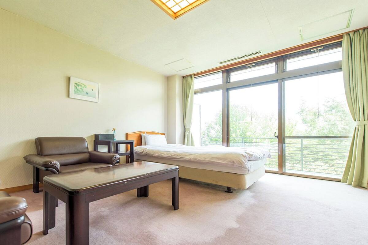 Una habitación de hotel con cama, sofá, mesa y un ventanal con cortinas.
