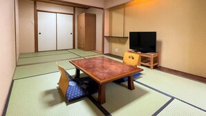 A traditional Japanese room with tatami flooring, a wooden table, a television on a stand, and sliding doors. - Dochu Land Shin Onsen (Awa)