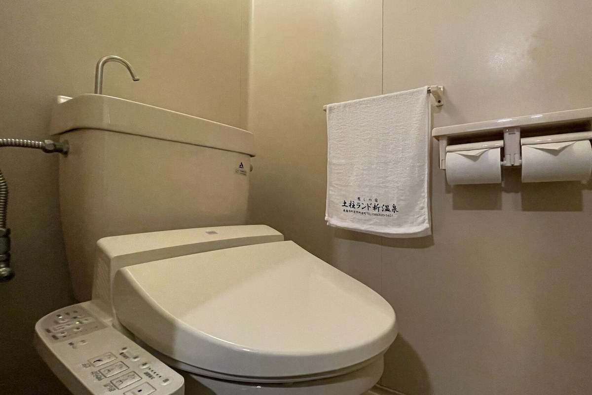 A bathroom with a toilet, a shower, and a towel rack with a towel.