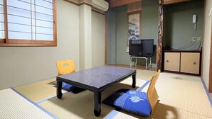 A tatami mat room with a low table, a television on a stand, and a futon bed. - Dochu Land Shin Onsen (Awa)