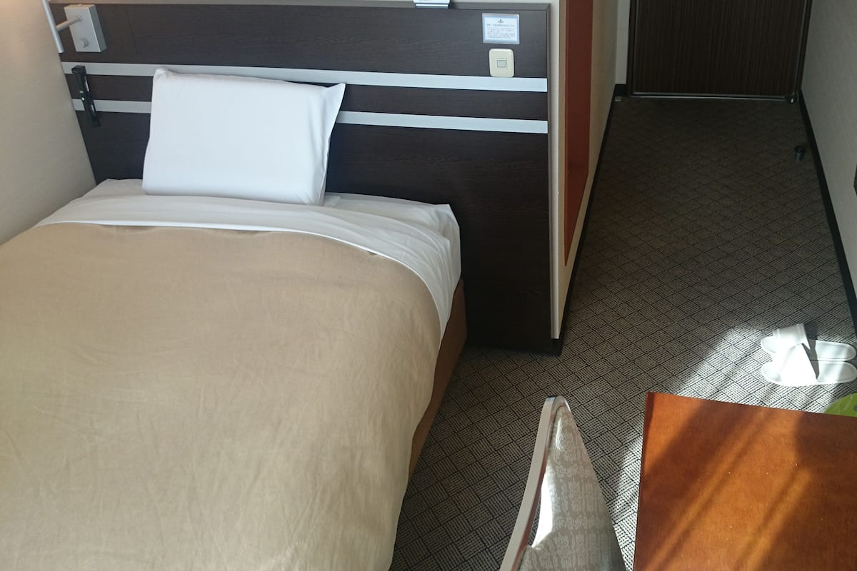 Een hotelkamer met een bed, nachtkastje, lamp en een klok aan de muur.