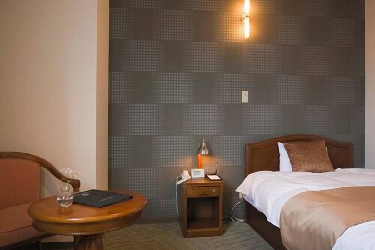 Ein Hotelzimmer mit Bett, Nachttisch, Stuhl und Wand mit Strukturmuster.