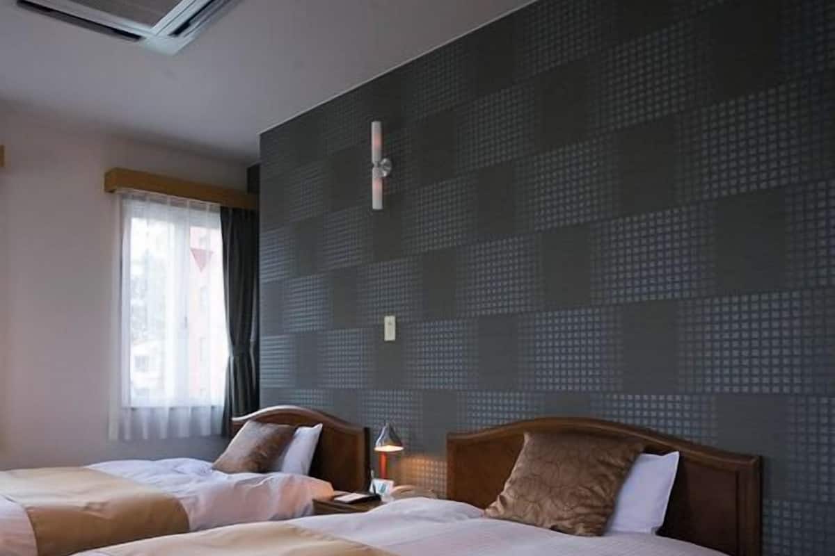 Ein Hotelzimmer mit zwei Betten, einem Fenster mit Vorhängen und einer strukturierten Wand.