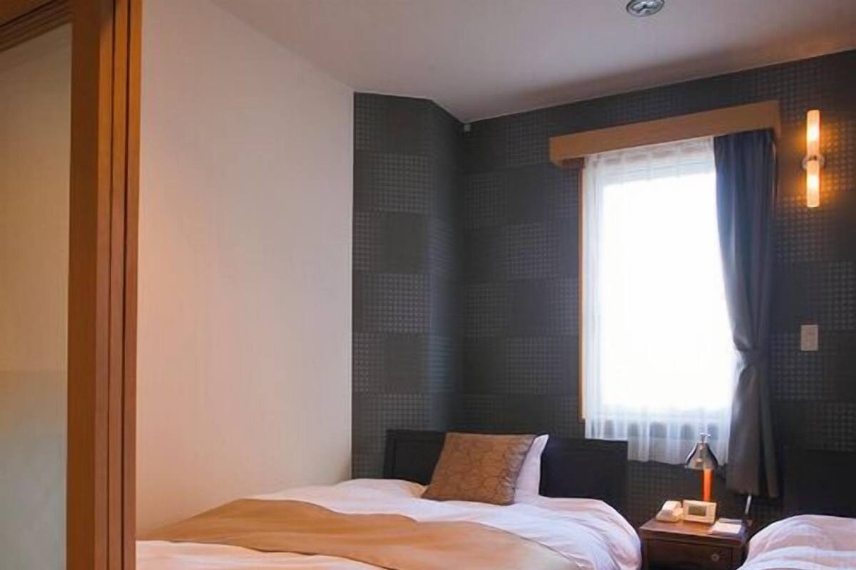 Ein Hotelzimmer mit zwei Betten, einem Nachttisch, einem Fenster mit Vorhängen und einer Wandlampe.