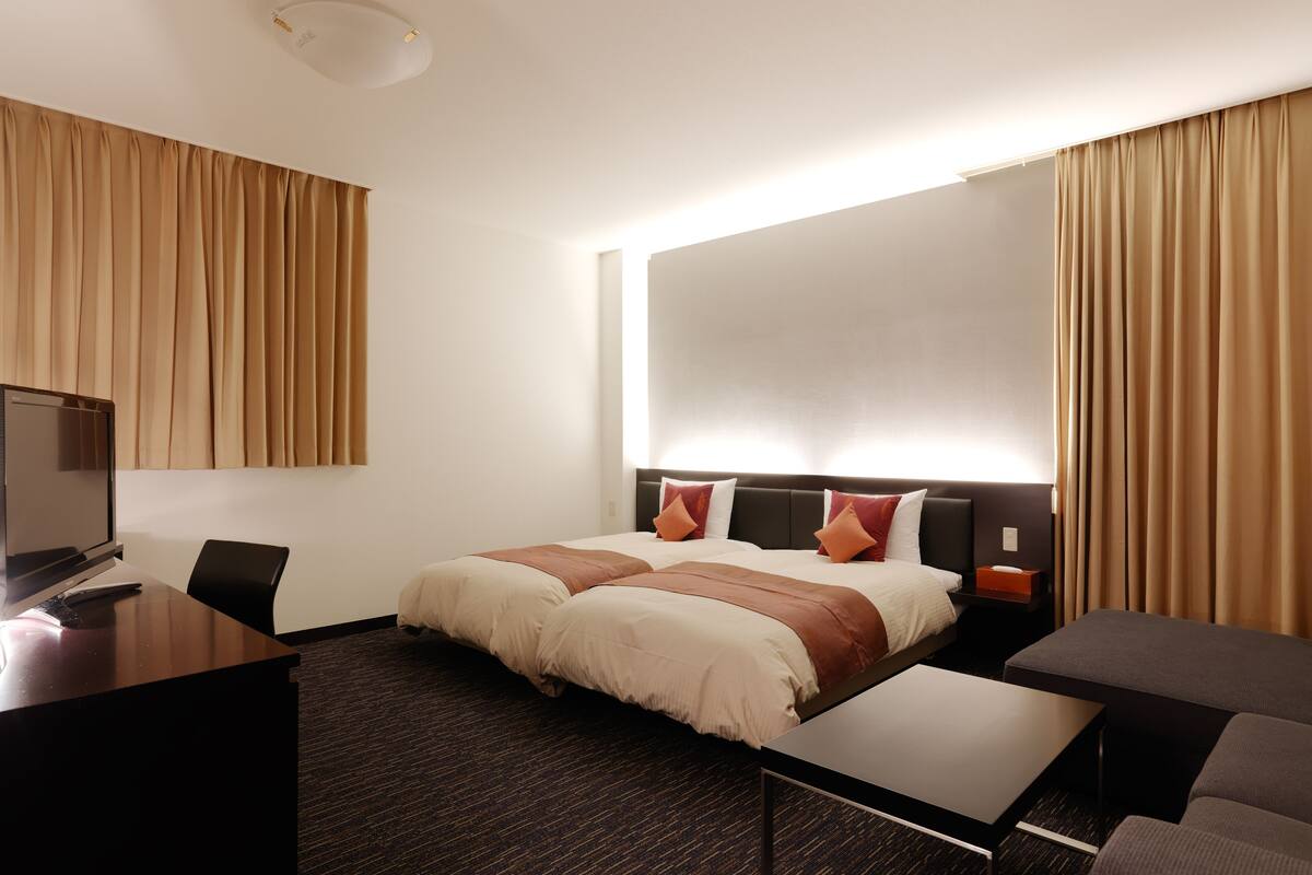 A hotel room with a bed, a desk, a chair, a TV, and curtains.