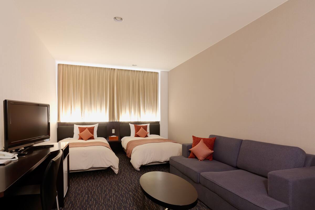 A hotel room with two beds, a sofa, a TV, and a desk.
