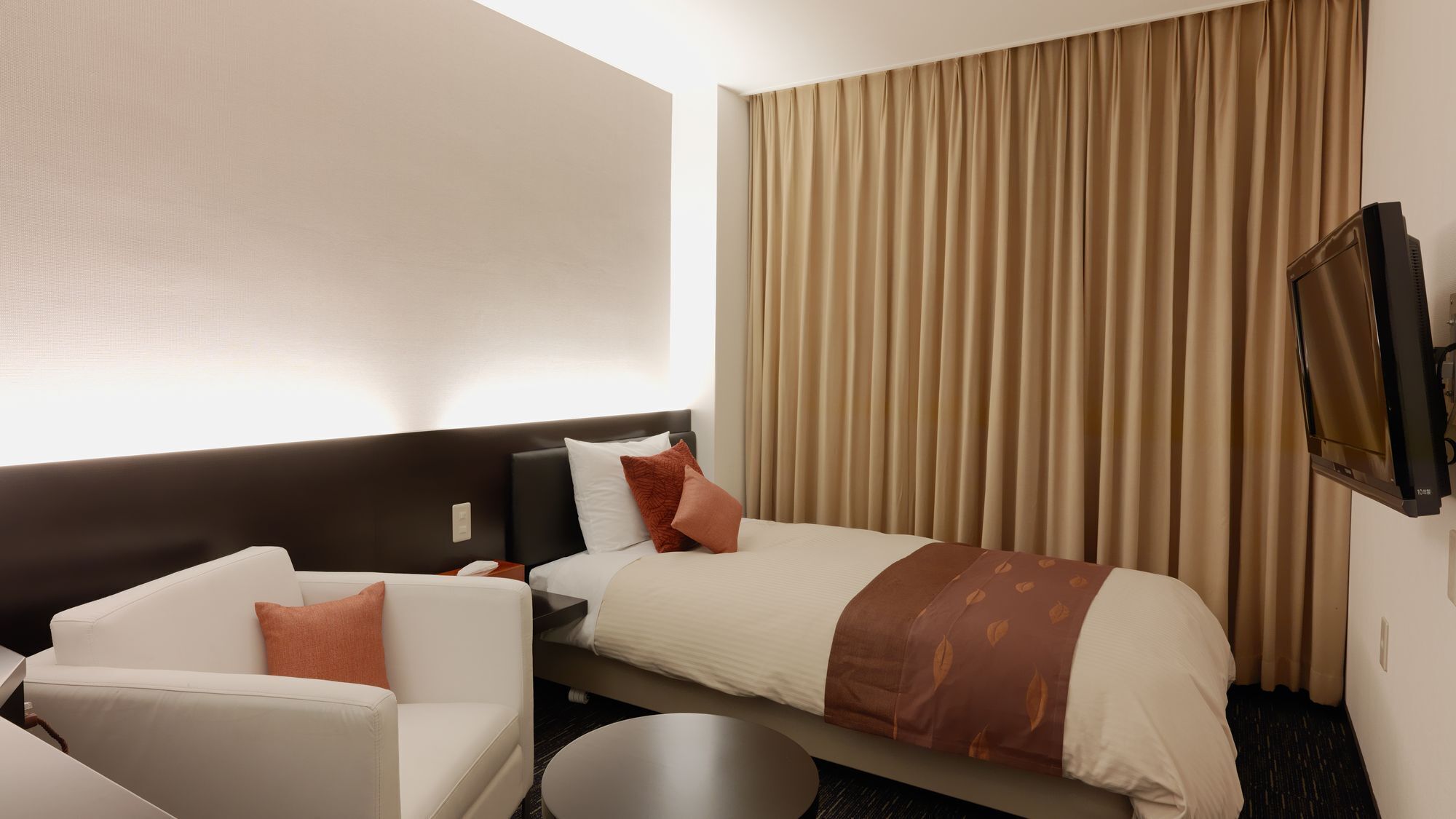 A hotel room with a bed, a sofa, a TV, and a curtain.