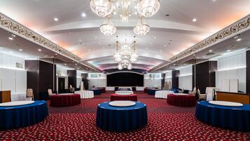 A spacious conference room with round tables, a stage, and ornate chandeliers.