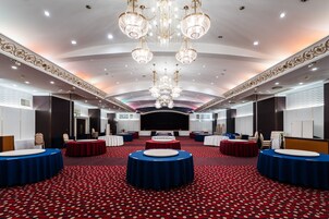 Una amplia sala de conferencias con mesas redondas, un escenario y lujosos candelabros.