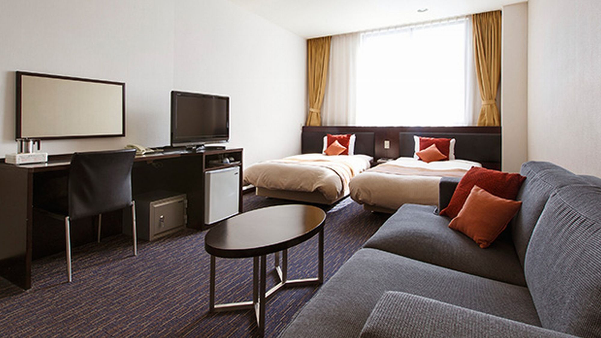 A hotel room with a desk, two beds, a sofa, and a TV.