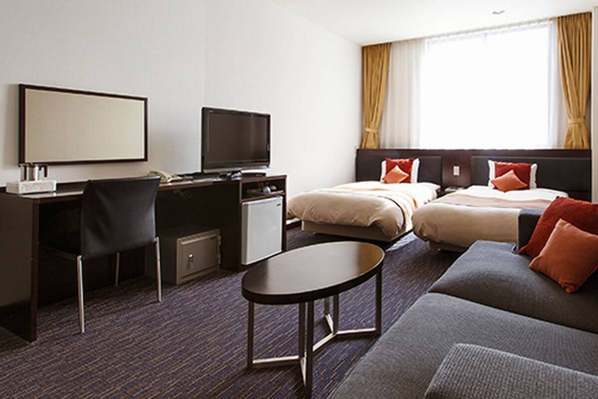 A hotel room with a desk, two beds, a sofa, and a TV.