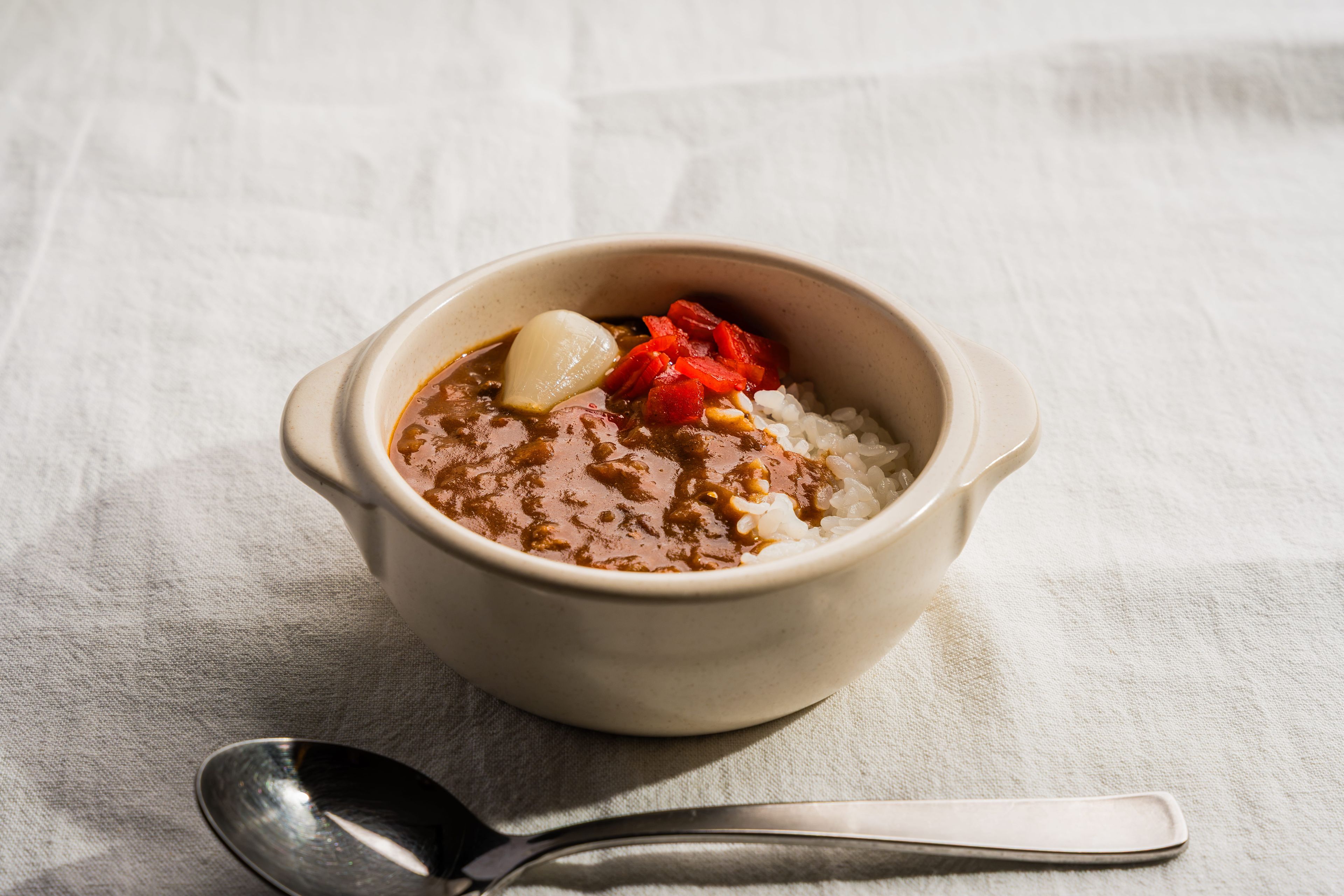Un plato de comida con arroz y salsa, sobre un paño blanco con una cuchara al lado.