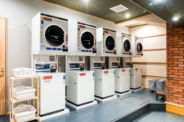 A row of white laundry machines with control panels, a wooden bench, and baskets on shelves.