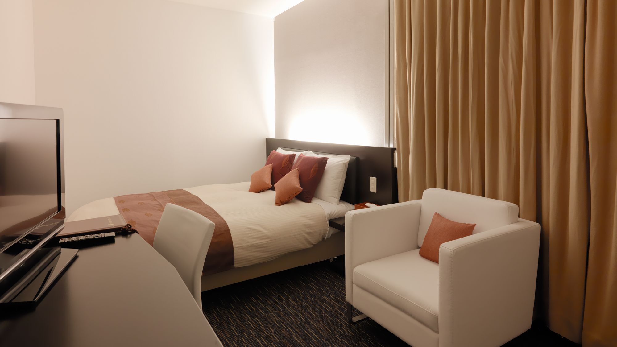 A hotel room with a bed, a desk with a television, a chair, and a curtain.
