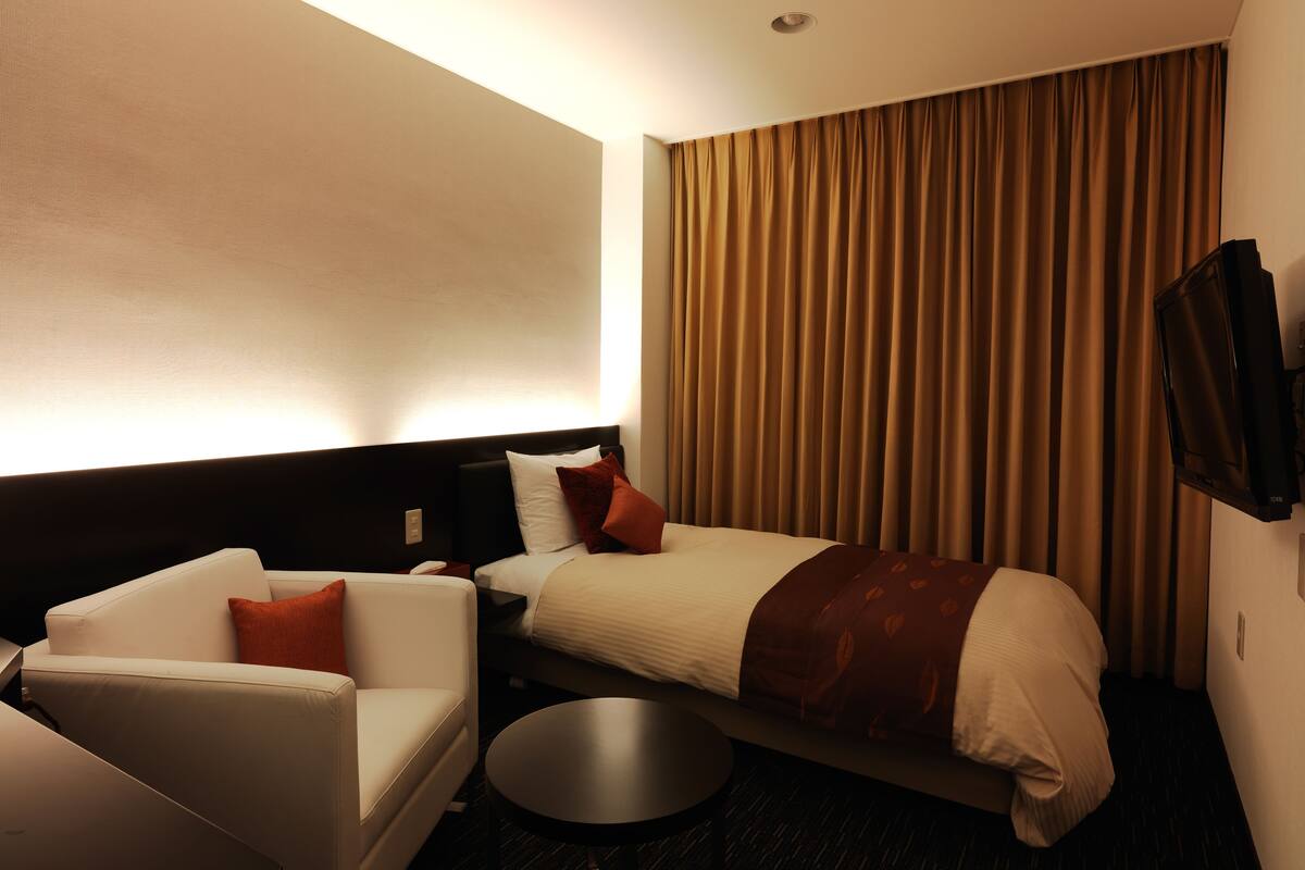 A hotel room with a bed, a sofa, a small table, and a TV mounted on the wall.