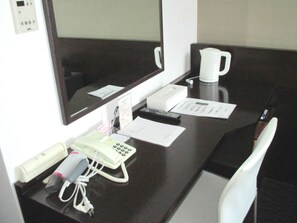 Mostrador de hotel con computadora, teléfono, cafetera y algunos documentos.