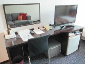 Habitación de hotel con escritorio, ordenador, teléfono, caja fuerte pequeña y espejo.