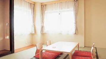 A room with a wooden table and four chairs, two red cushions on the floor, and a window with curtains.